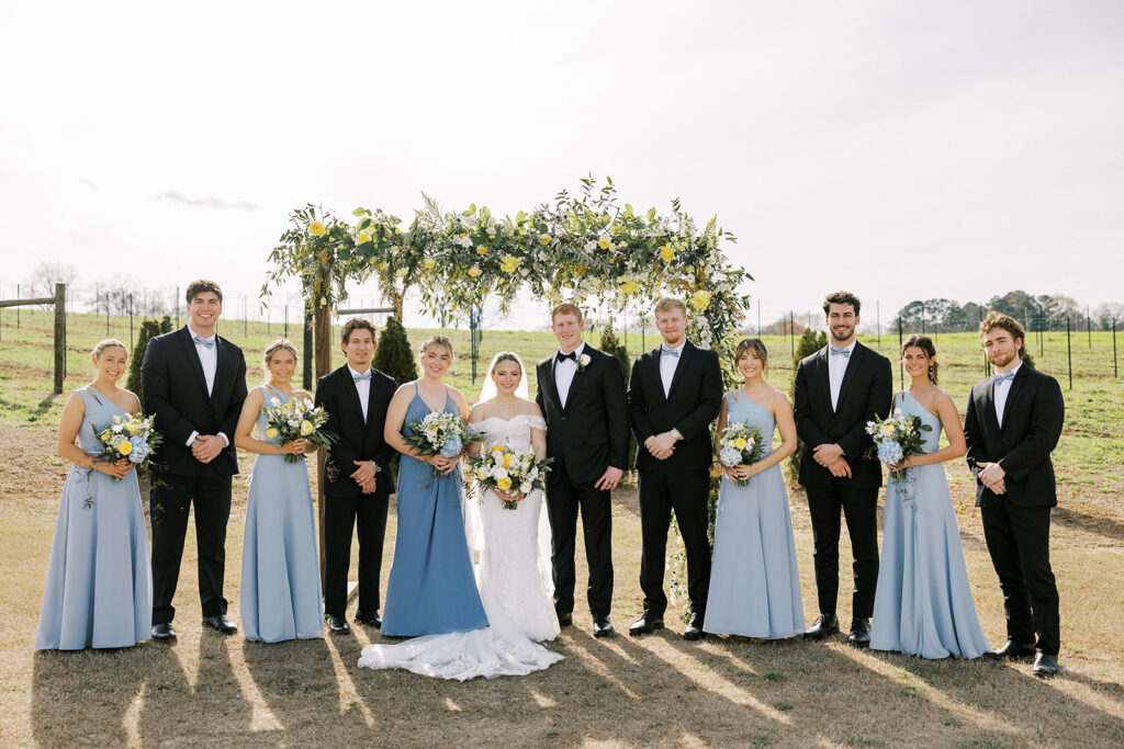 The bride and groom stand with close family members after a wedding in front of the wedding arbor at an outdoor wedding venue near Atlanta GA.