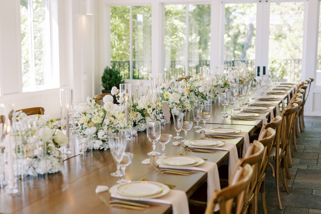 Gorgeous floral arrangements line the wedding party head table inside the covered enclosed patio space with candlelight and beautiful china at a wedding venue near Atlanta