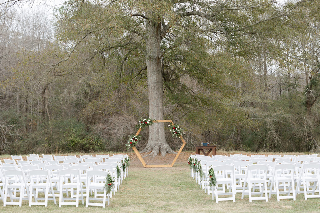 The Big Oak Tree ceremony site with a wooden hexagon arbor adorned with beautiful fresh floral swags and a unity ceremony table at the altar with white padded resin chairs with floral swags at Murphy Lane