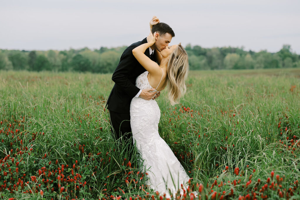 Newlywed couple kissing in an open crimson clover field at an outdoor wedding venue near Atlanta