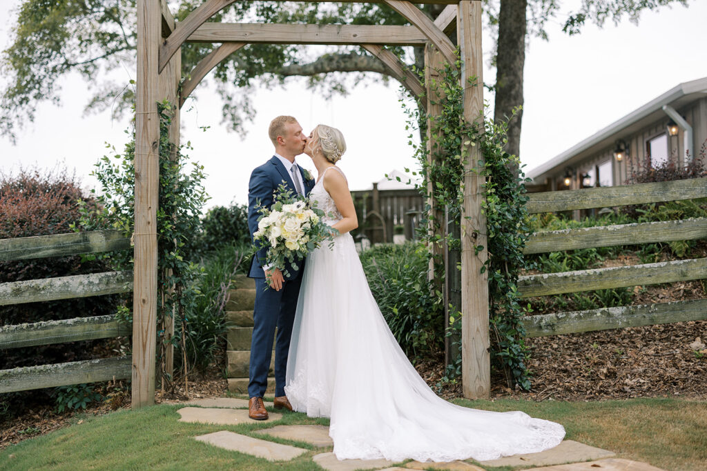 First look photos for bride and groom by local photographer at an outdoor arbor with bridal bouquet at a wedding venue near Atlanta