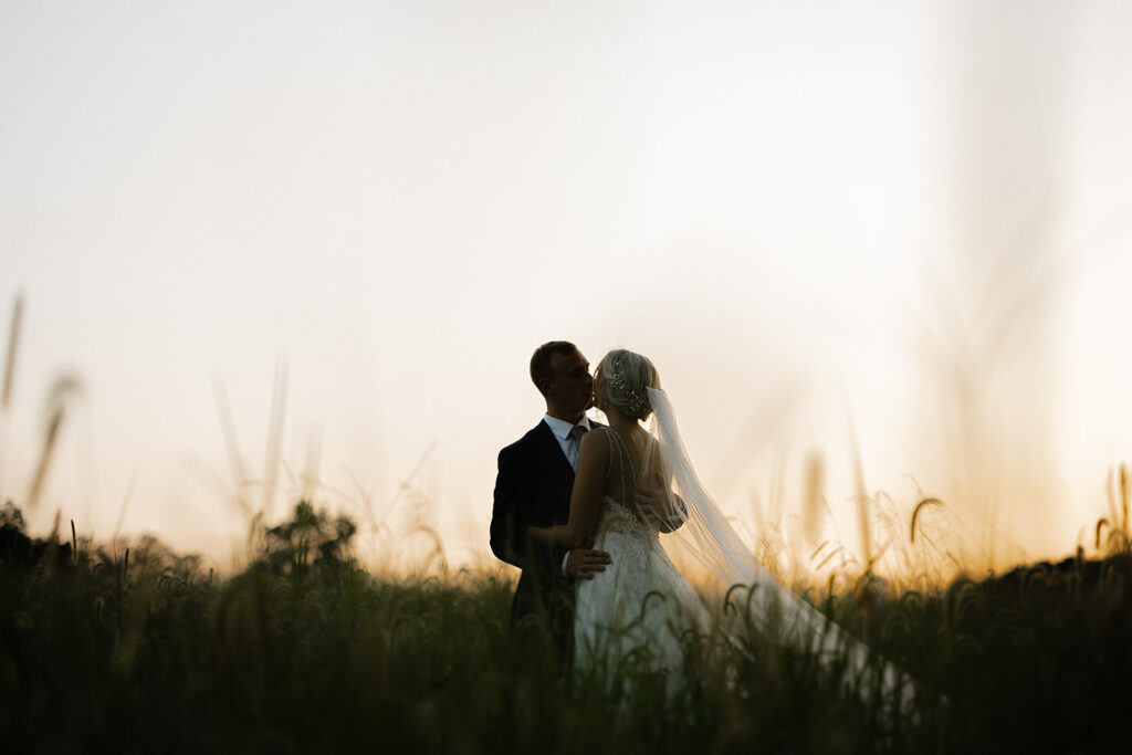 Bride and groom in a field with photographer at sunset on wedding day at The Venue at Murphy Lane