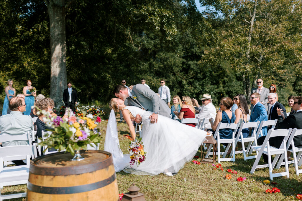 Beautiful wedding ceremony site at the Big Oak Tree located at an outdoor wedding venue close to Atlanta, GA with the bride and groom coming down the wildflower lined aisle and guests watching as they kiss