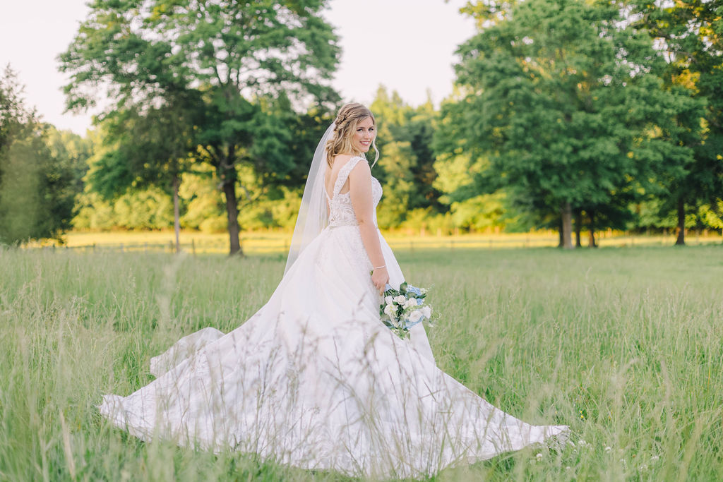 Gorgeous bride in her wedding dress holding her bridal bouquet in a field located at a wedding venue with a vineyard near Atlanta