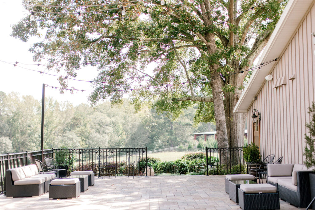 Outdoor open air patio with pavestone floor and hanging bistro lights and outdoor lounge furniture at a wedding venue with a vineyard located near Atlanta 