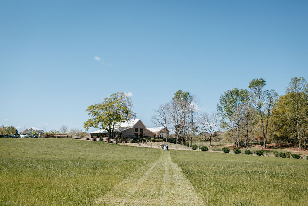 The barn in the background as the bride and her father get ready to walk down the aisle through the tall grass hayfield towards the Big Oak Tree ceremony site at The Venue at Murphy Lane