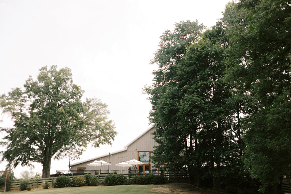 The North patio nestled among the big old trees on the patio space decorated with outdoor umbrellas and furniture with bistro lighting and looks down upon the valley wedding ceremony site at The Venue at Murphy Lane located in Newnan, GA which one hour south of Atlanta, GA